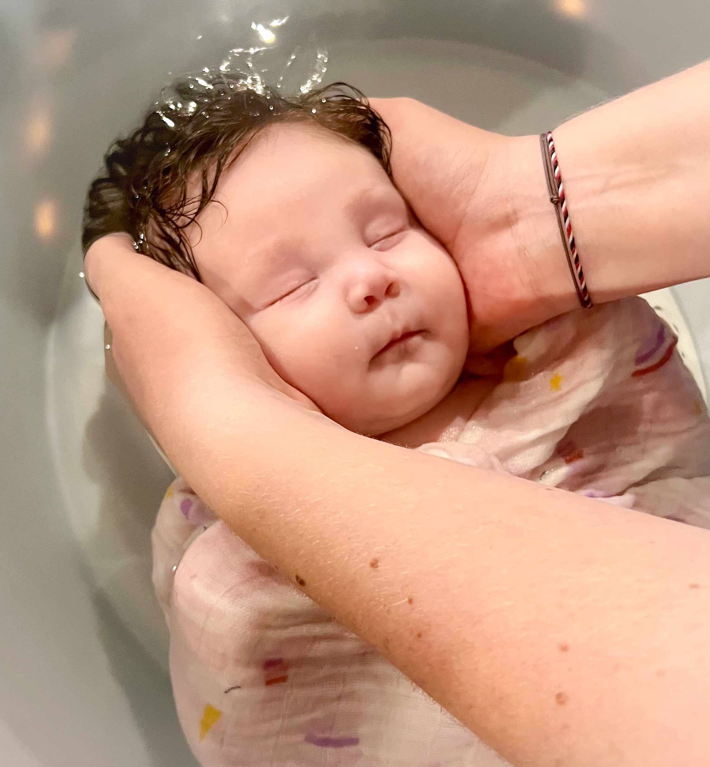 Nouveau-né apaisé pendant son bain sensoriel, tenu dans les mains