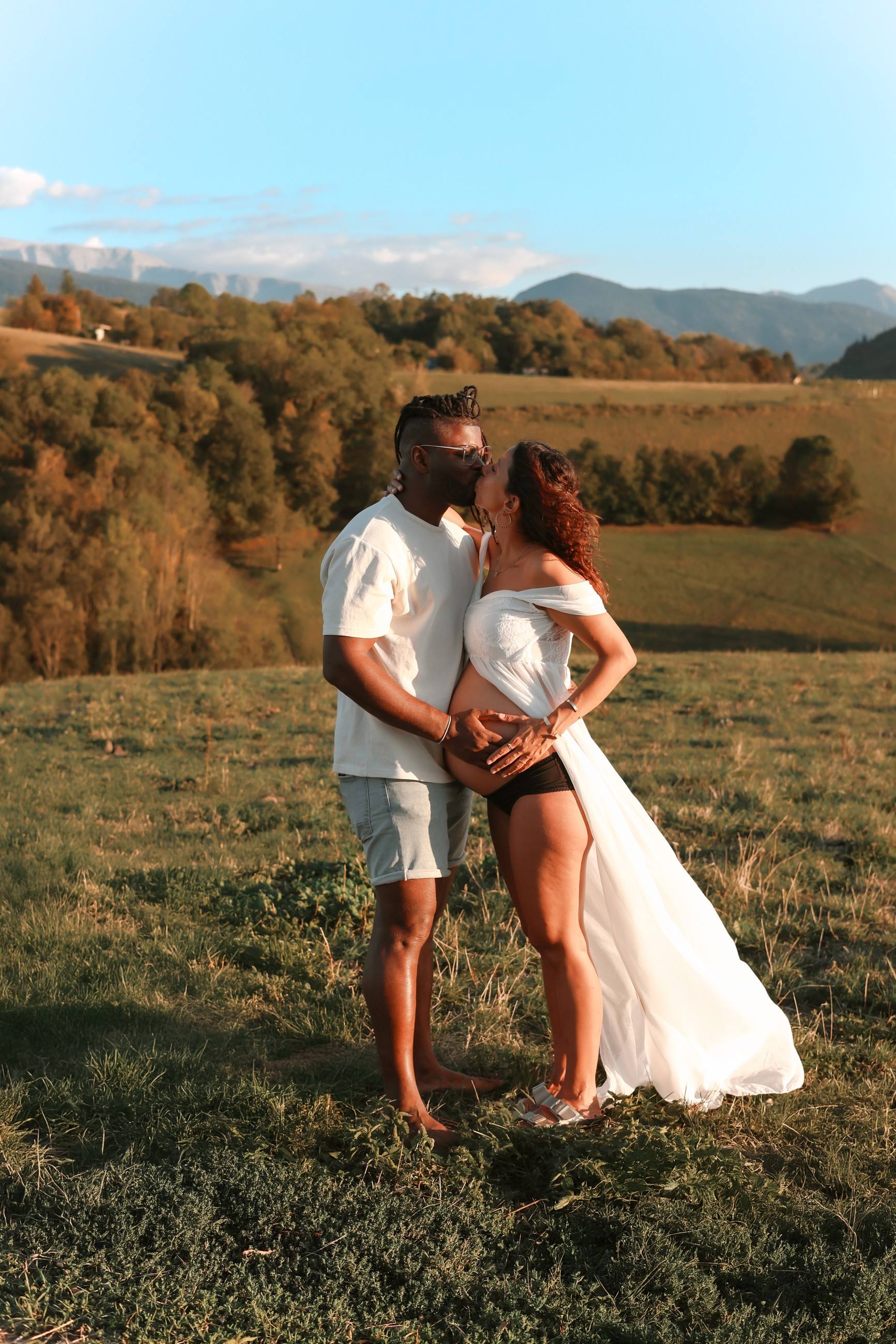 Baiser des futurs parents dans une prairie face aux montagnes