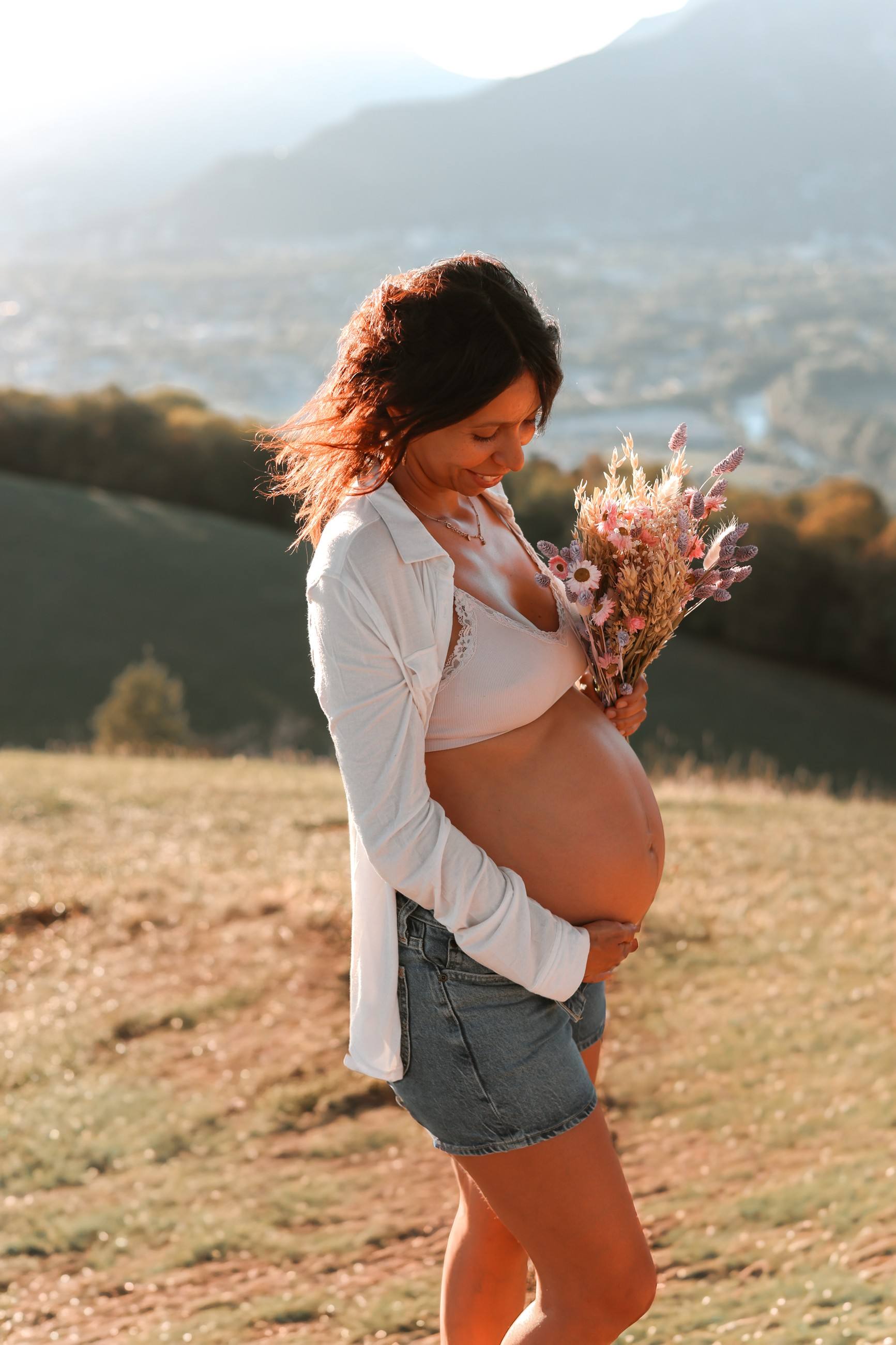 Femme enceinte tenant un bouquet de fleurs séchées sur une colline