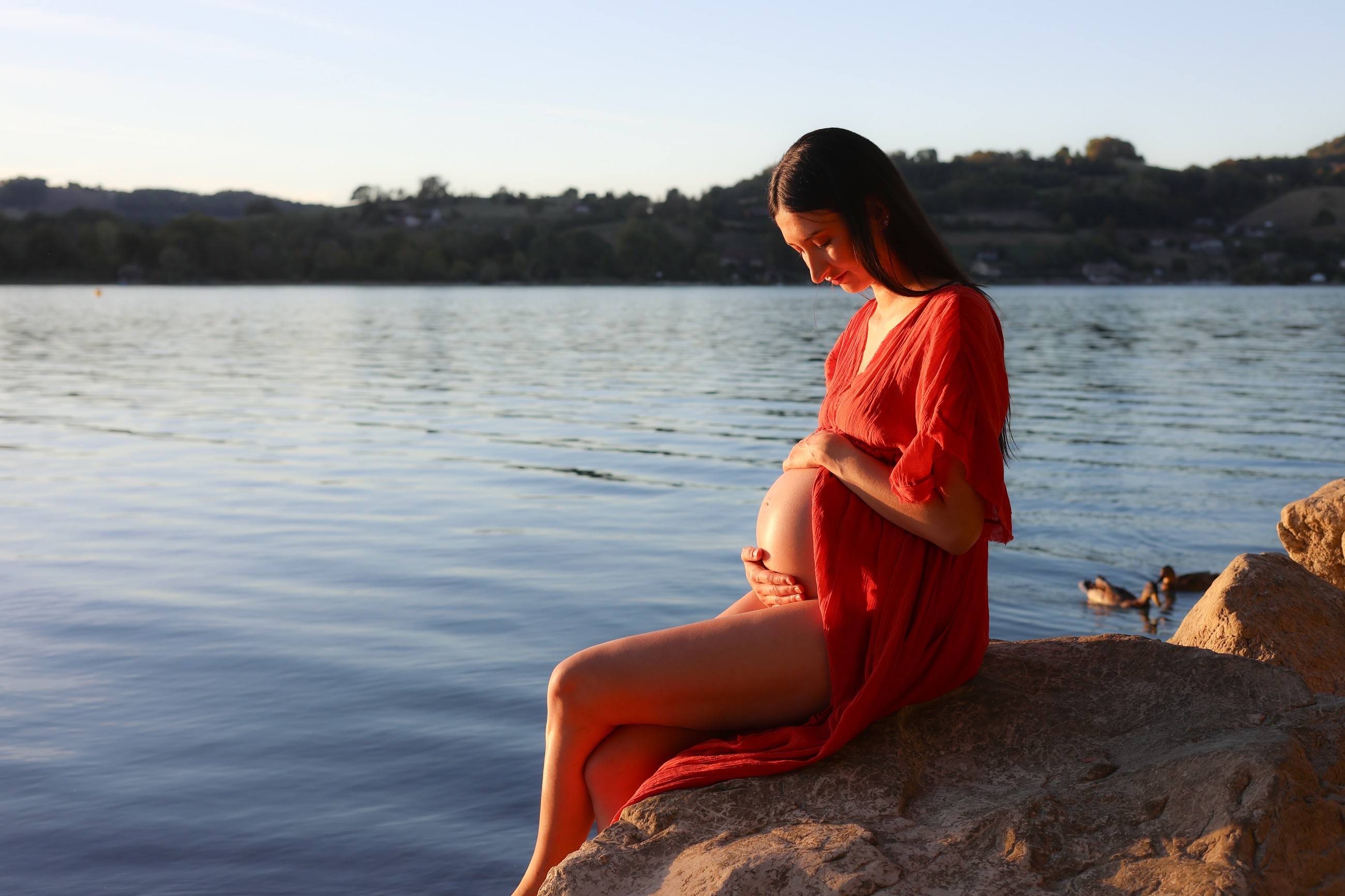 Femme enceinte en robe rouge au bord d’un lac en Isère
