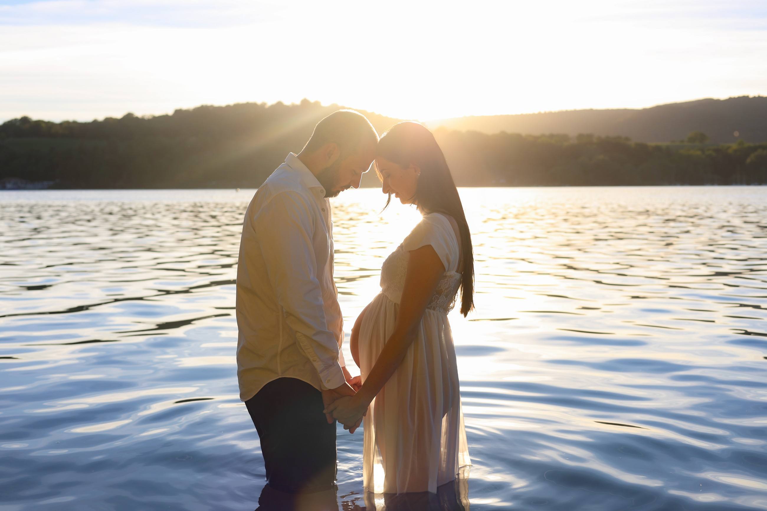 Couple de futurs parents dans un lac au coucher du soleil